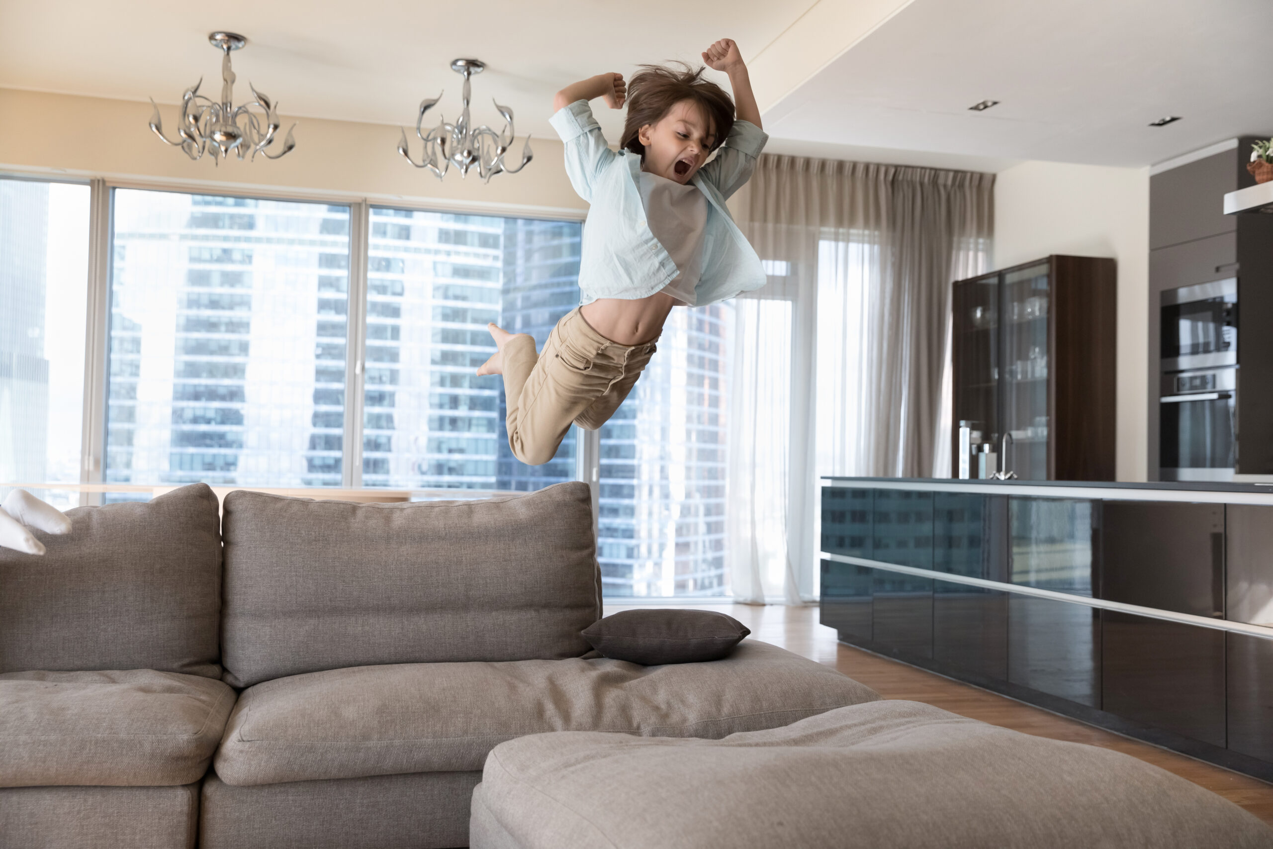 Excited crazy boy kid jumping on big sofa