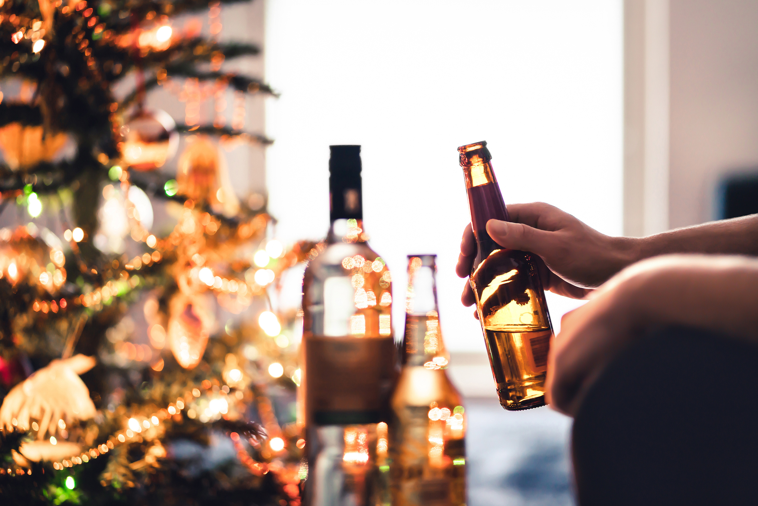 Christmas party with alcohol bottles. New year's celebration. Beer, wine and vodka. Festive Xmas tree. Alcoholism and drinking problem concept. Lonely unhappy man with beverage and cocktail in winter.