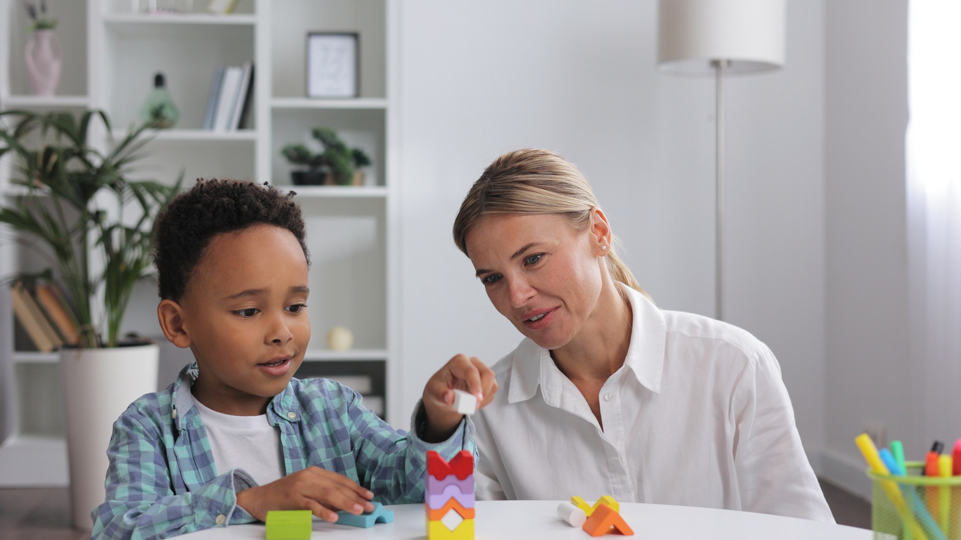 Assessment of mental development of children. Professional psychologist observes small multiracial boy playing with puzzle game, assessing his readiness for preschool. Exercises for kid with autism.